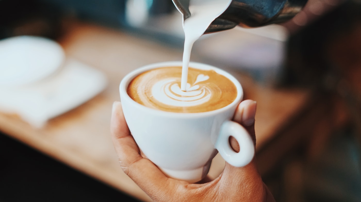 A latte poured tableside, crema and steamed milk swirling into the cup
