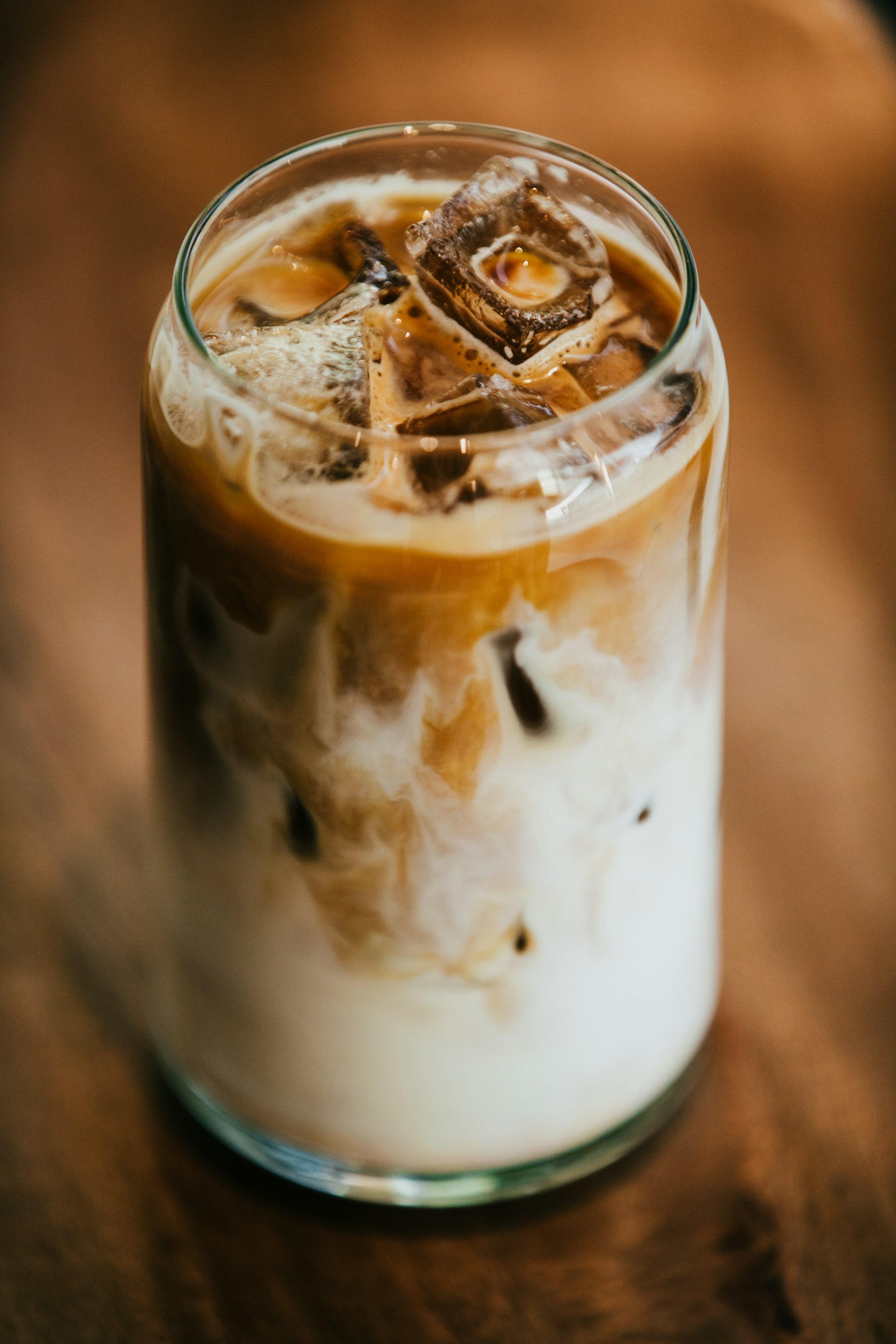 Iced barako coffee with cream swirled through it, in a tall glass on a wooden table