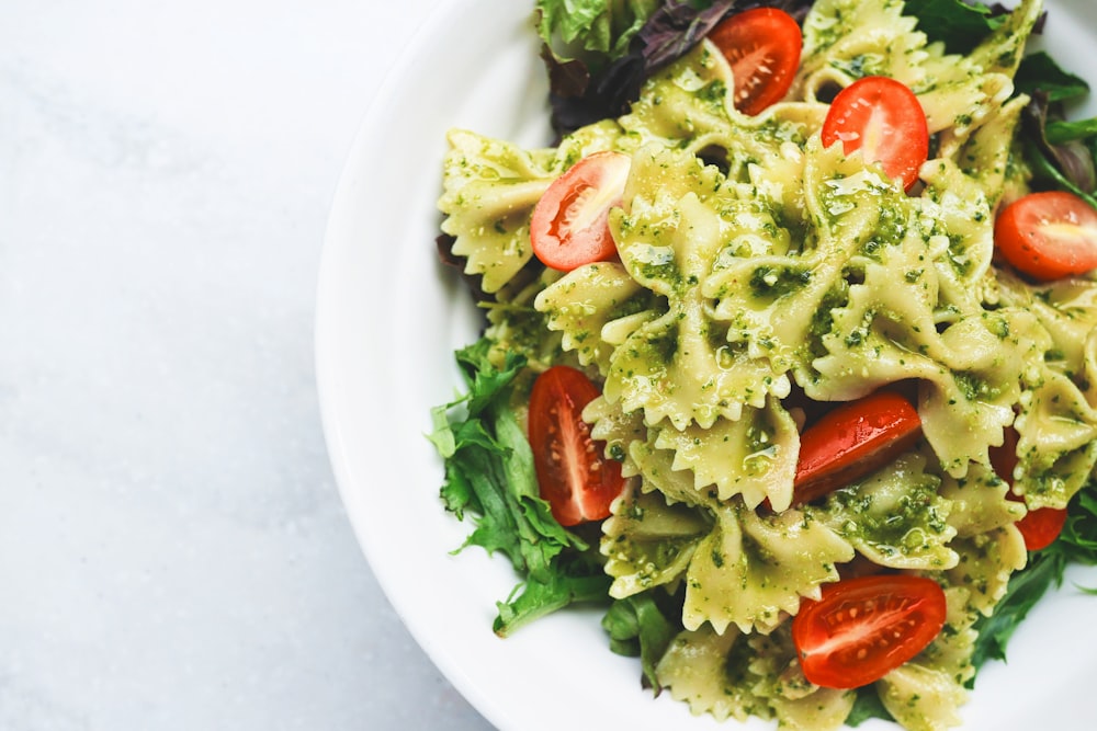 A bowl of pesto pasta with cherry tomatoes and greens