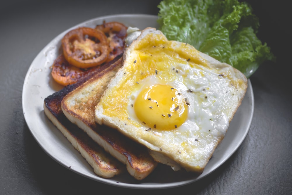 A fried egg over toast with grilled tomato and lettuce on a plate