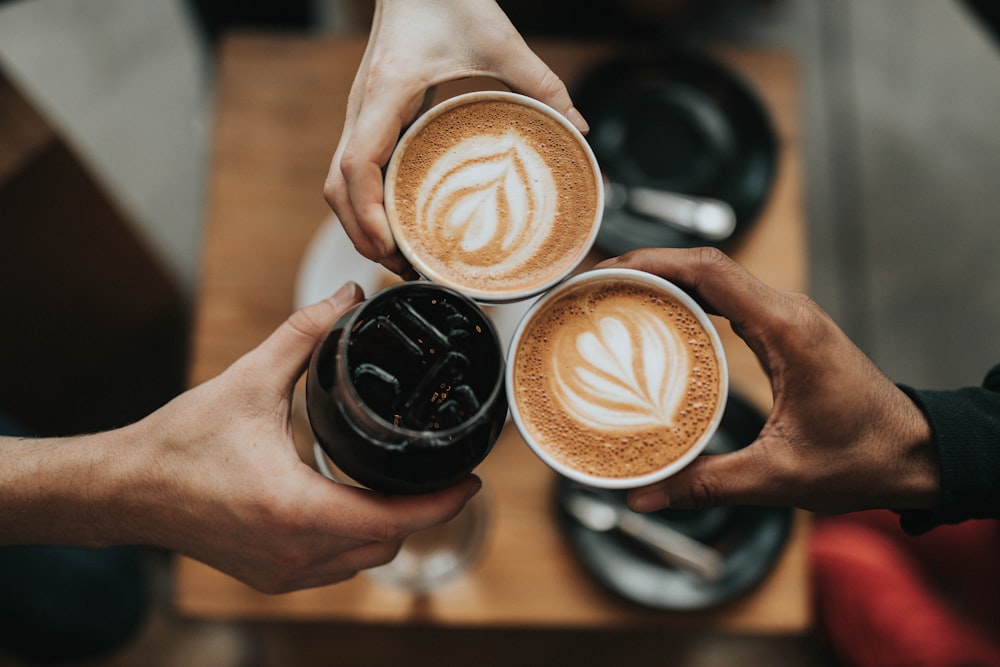 Three latte-art coffees held together in a toast