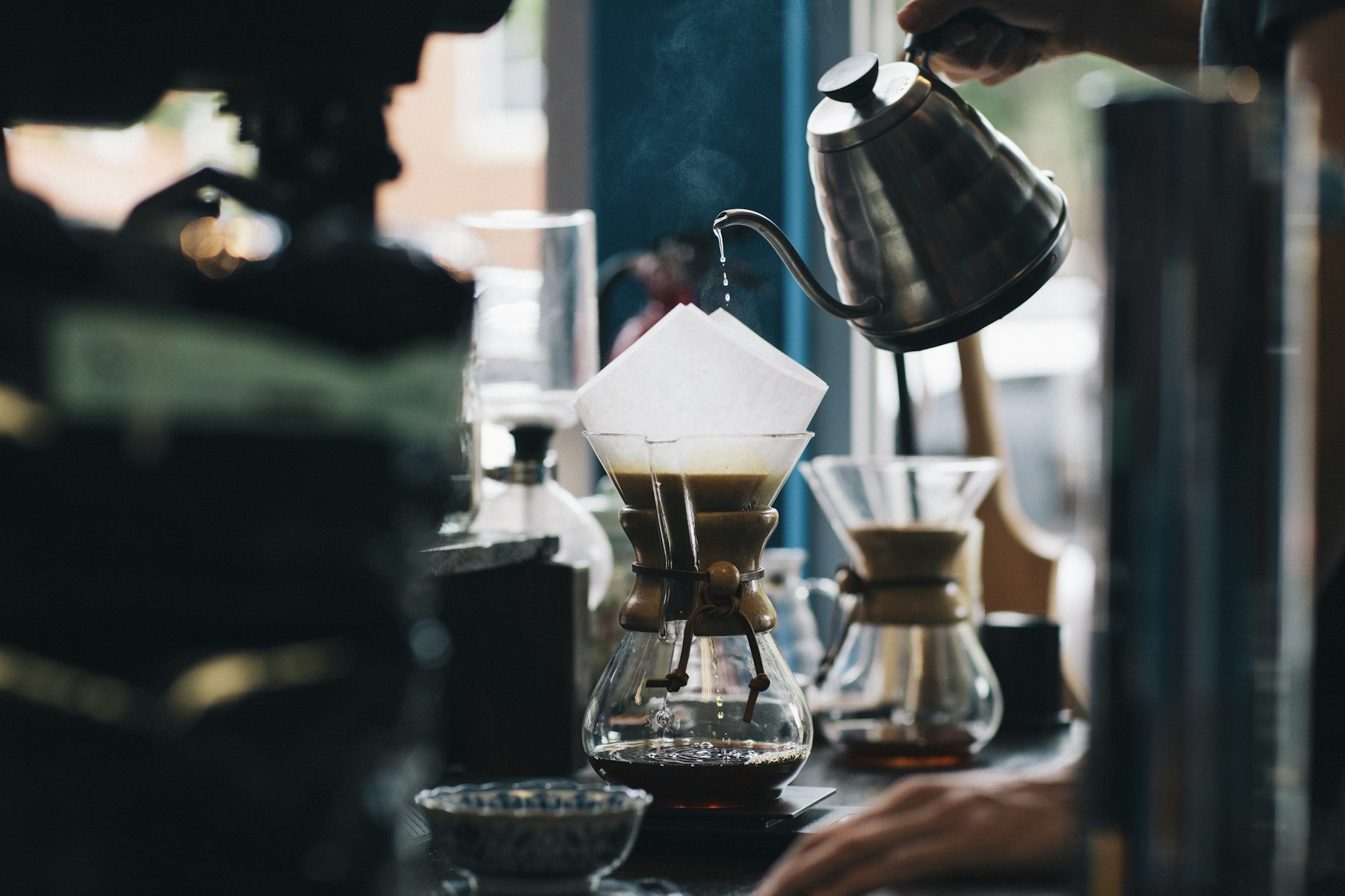 Hot water poured slowly over coffee grounds in a pour-over, steam rising in warm light
